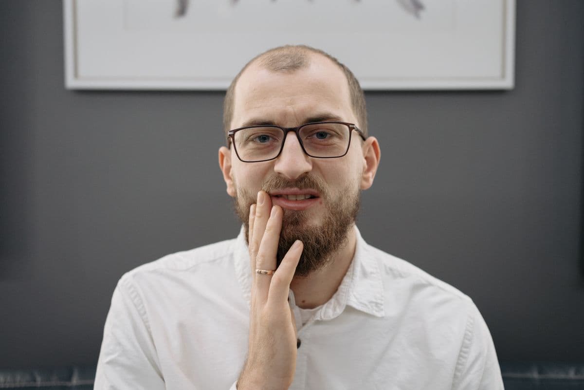 Man with glasses holding his jaw in pain, indicating severe toothache