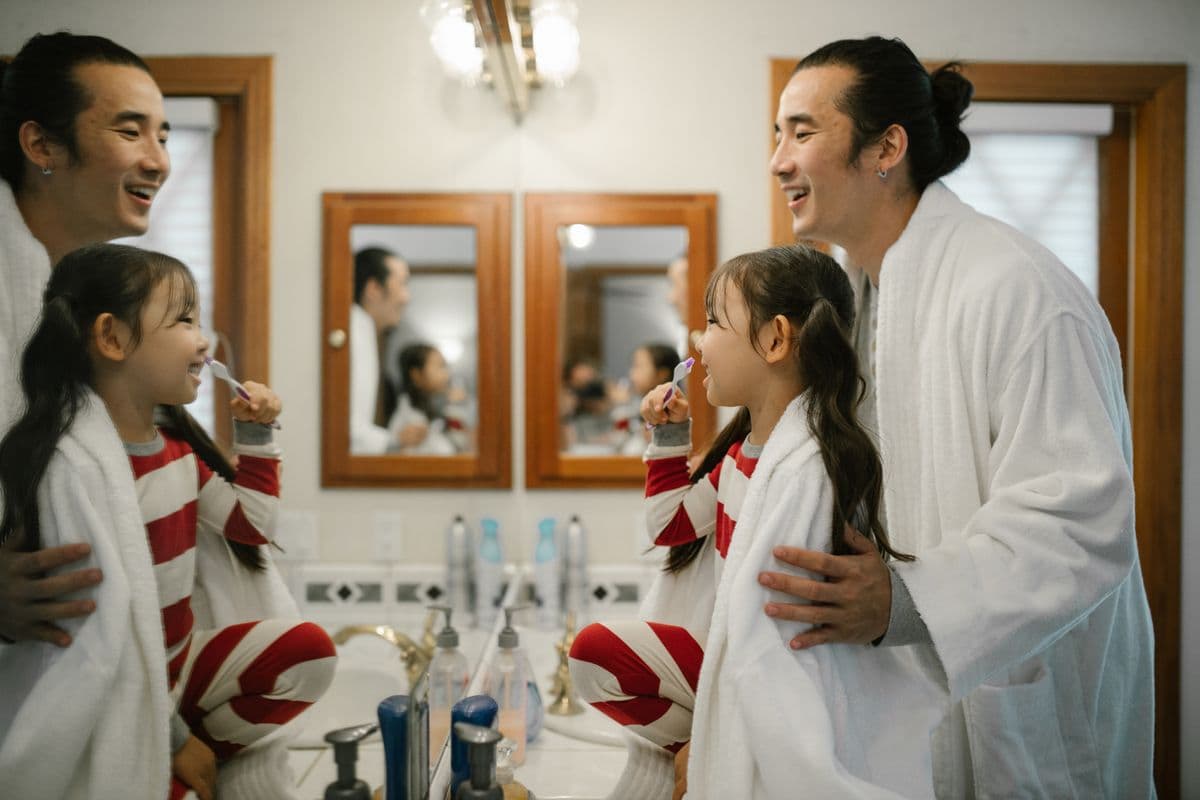 Parent and child brushing their teeth together in front of a bathroom mirror
